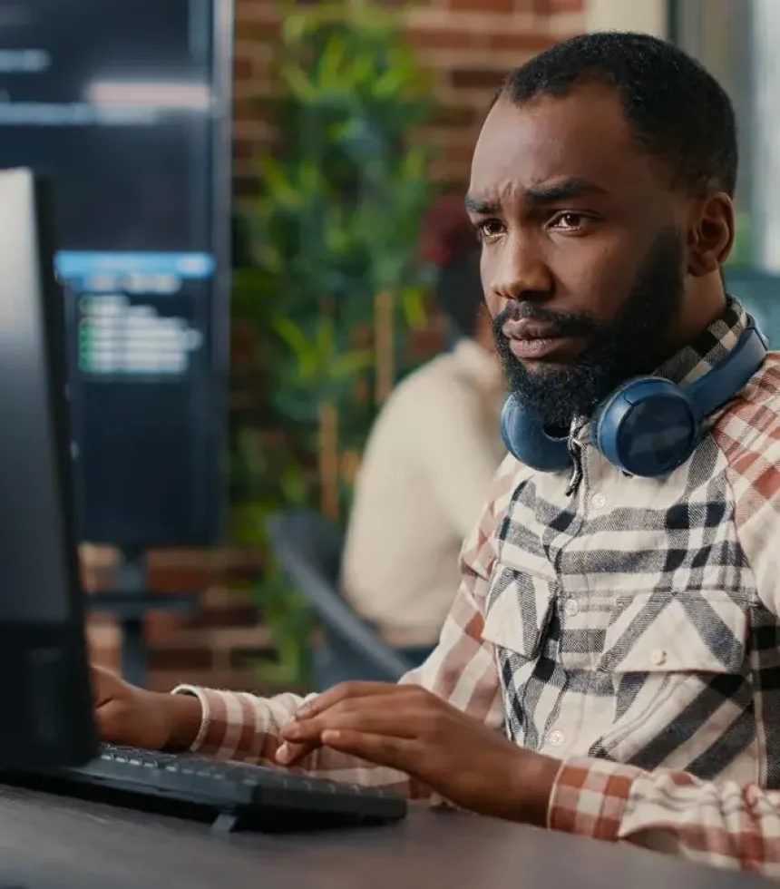 portrait-focused-african-american-programer-wearing-wireless-headphones-working-looking-computer-screen-while-typing-software-developer-writ